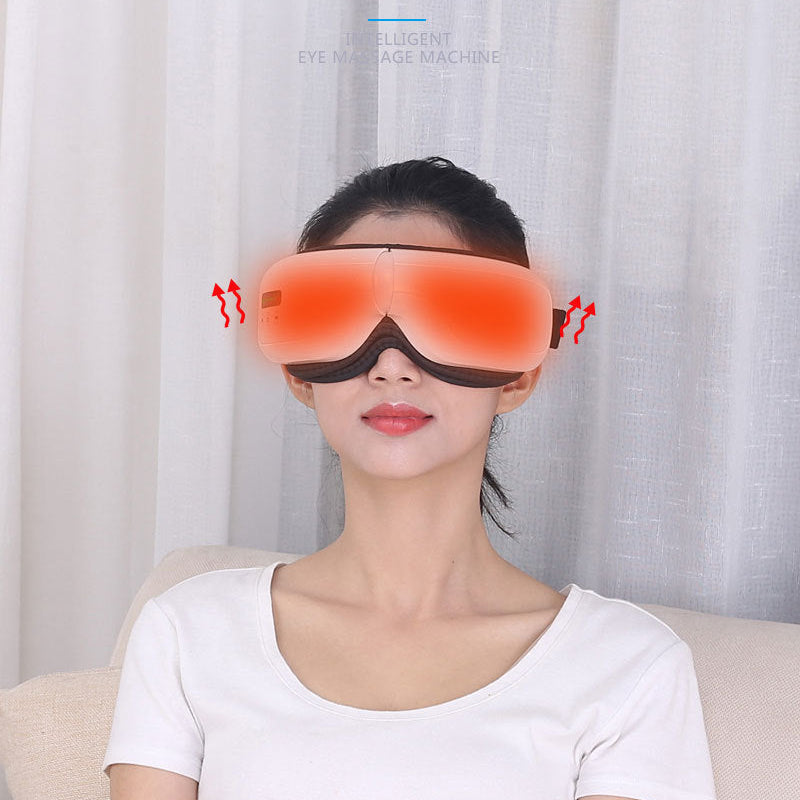 A woman wearing a red eye massager and a white t-shirt is sitting on a beige sofa in front of white curtains.
