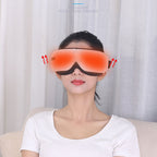 A woman wearing a red eye massager and a white t-shirt is sitting on a beige sofa in front of white curtains.