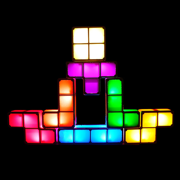 A pyramid-shaped arrangement of glowing light-up block tiles in multiple colors, including yellow, orange, pink, purple, green, and blue, set against a solid black background.